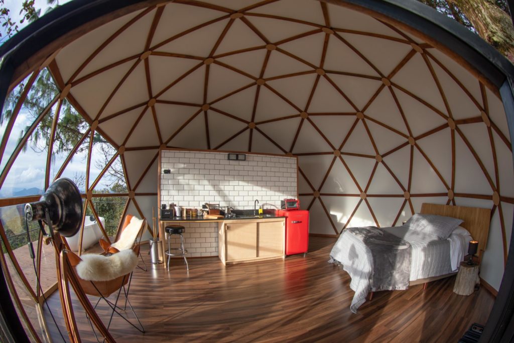 Visão interior de domo geodésico em São Paulo com cama de casal, cozinha completa, frigobar e poltronas